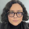 Giselle Garcia, a person with short wavy black hair and glasses, looks at the camera.