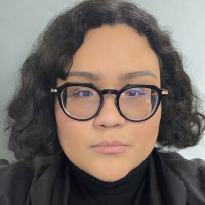 Giselle Garcia, a person with short wavy black hair and glasses, looks at the camera.