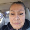 Nancy Torres, a woman with brown hair pulled back, looks at the camera in a selfie. She is sitting in a car with grey seats, and wearing a dark colored jacket.